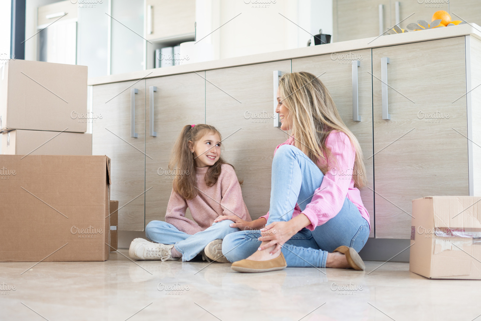 Mother and daughter sitting on kitchen floor among moving boxes in new home, a Person Photo by etorres69