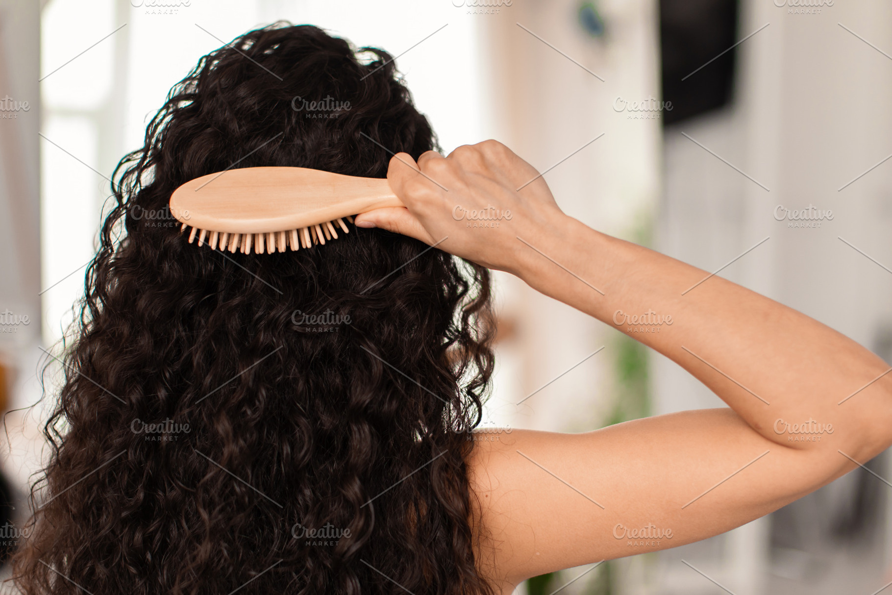 Back view of young brunette woman brushing her long wavy hair with wooden brush, a Photo by Prostock-Studio