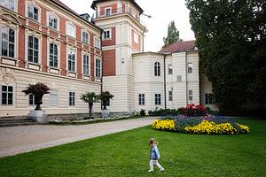 A historic building in Lancut, Poland with a colorful garden and child, a Photo by AS photostudio
