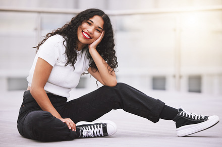 Beautiful mixed race fashion woman sitting outside in the city during the day. Young hispanic woman looking stylish and trendy, smiling and happy while outdoors in summer. Carefree and fashionable, a Photo by Peopleimages.com