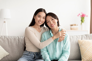 Portrait of young Asian woman and her mature mother hugging and smiling at came, a Photo by Prostock-Studio