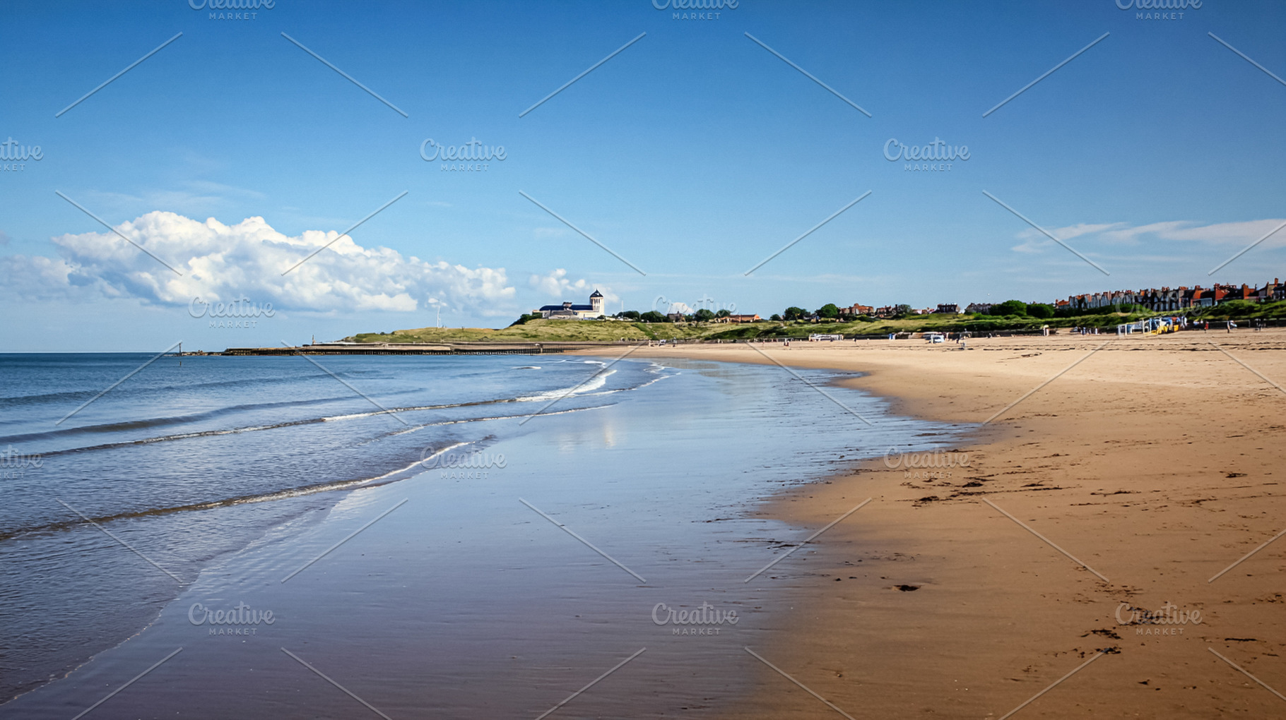 Wide sandy beach with gentle waves on a sunny day. Coastal town, a Photo by Studio ANNA