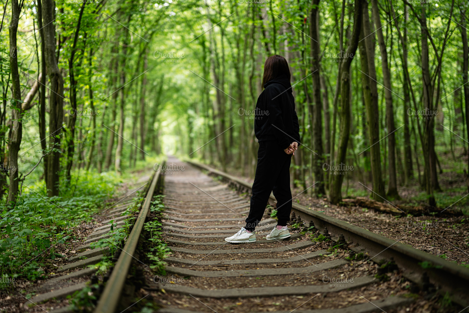 Woman standing on a railway surrounded by a lush green forest, a Photo by AS photostudio