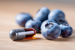 Dark-colored capsule placed beside fresh blueberries on a wooden surface, a Photo by AlyaAnd