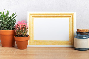 Empty frame mockup with cacti and blue jar on wooden table, a Background Photo by Olena Rudo