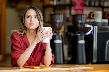 young woman in a red dress with a cup of coffee sits at a table, a Person Photo by Masson Simon