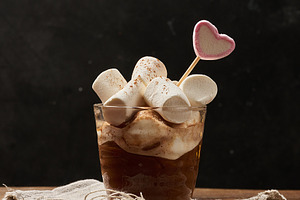A glass of hot chocolate with fluffy marshmallows on a wooden ta, a Food & Drink Photo by ndanko