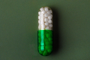 Close-up of a green and white capsule pill on a textured green background, symb, a Health & Medical Photo by Ales Munt
