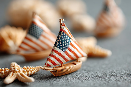 Miniature sailboats with American flags on a textured surface near seashells, a Holiday Photo by AlyaAnd