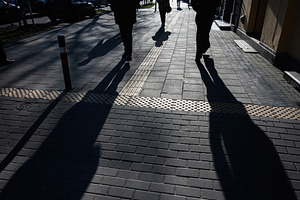 Shadows of pedestrians on sunlit urban sidewalk with textured tactile paving, a Photo by AS photostudio