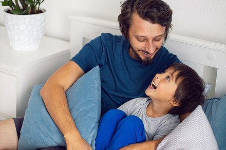 boy child and his father are sitting on the bed in the bedroom and laughing at, a Person Photo by SaulichPhoto