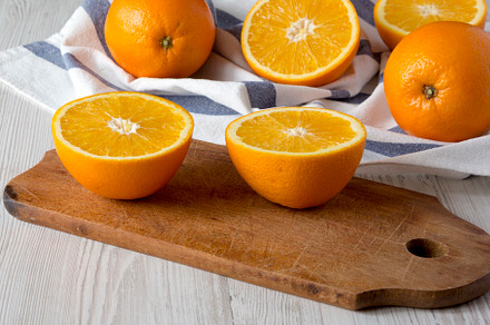 Halved and whole oranges on a white wooden background, side view, a Food & Drink Photo by LiudmylaChuhunova
