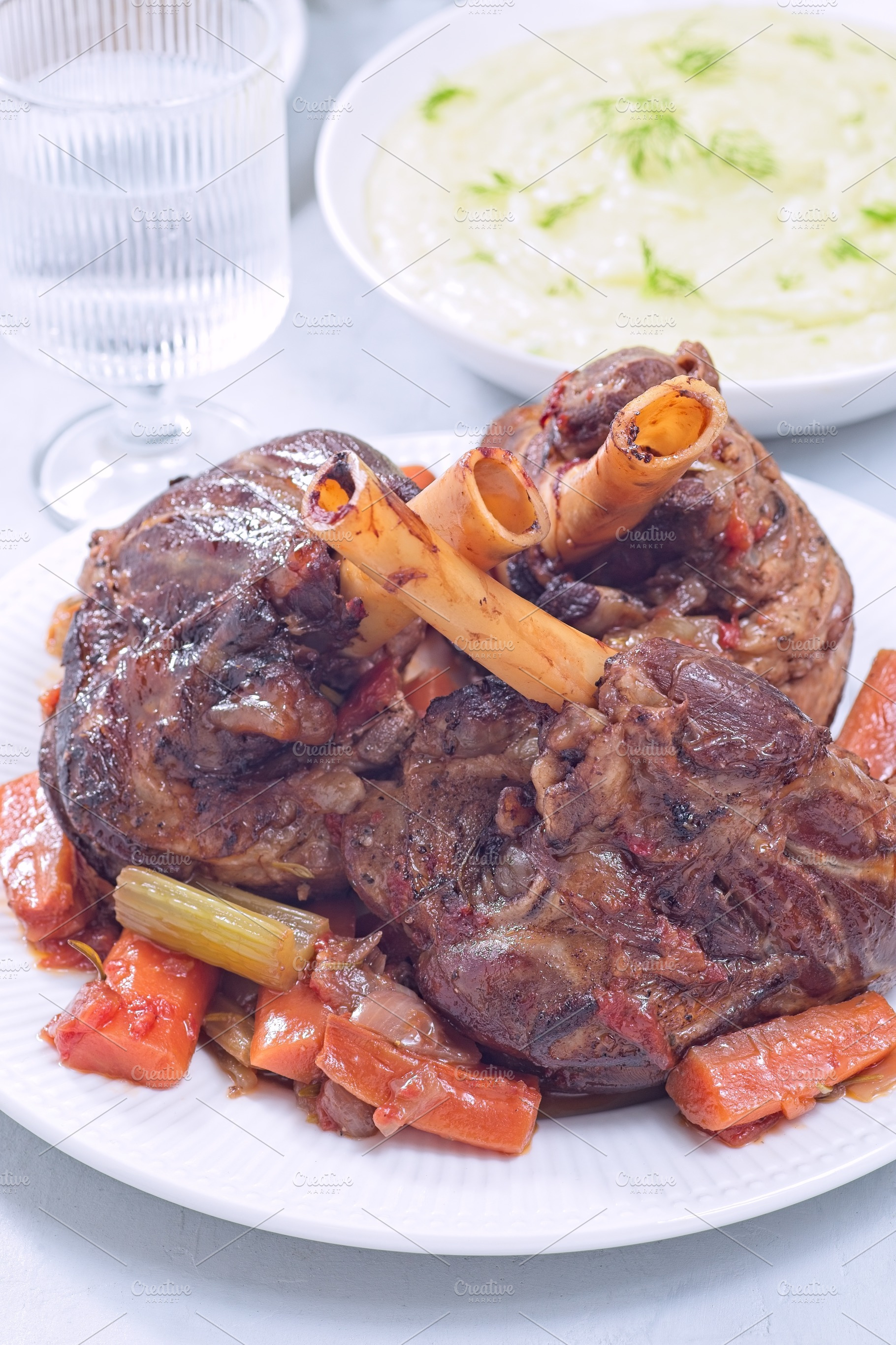 Braised lamb shanks with vegetables on a white plate, vertical closeup, a Food & Drink Photo by iuliia_n