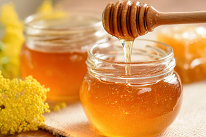 Golden honey dripping from dipper into small jar, surrounded by, a Photo by Studio ANNA