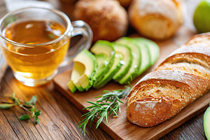 Sliced avocado and fresh bread served with herbal tea on a wooden table, a Food & Drink Photo by AlyaAnd