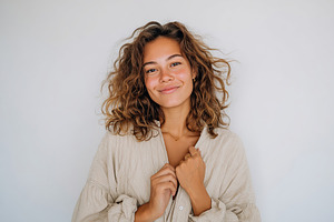 Happy young woman smiling in casual attire against a light background, a Photo by AlyaAnd