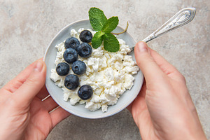 Hands holding bowl of cottage cheese, blueberries, mint, a Food & Drink Photo by Olena Rudo
