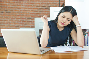 Asian woman thinking and serious in front of laptop in modern office