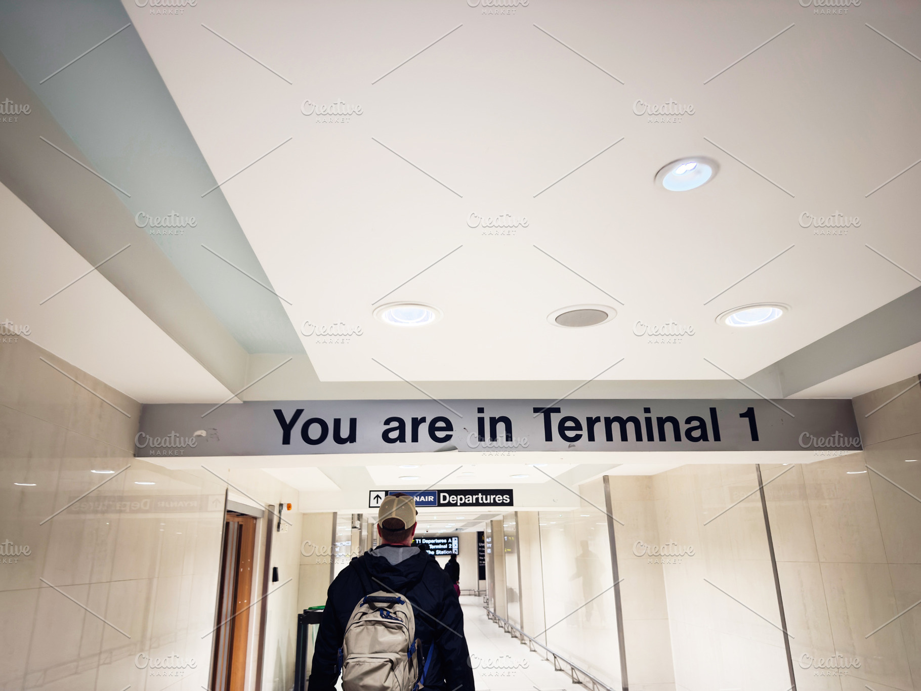 Traveler walks through a bright Manchester airport corridor beneath the You are, a Photo by AS photostudio