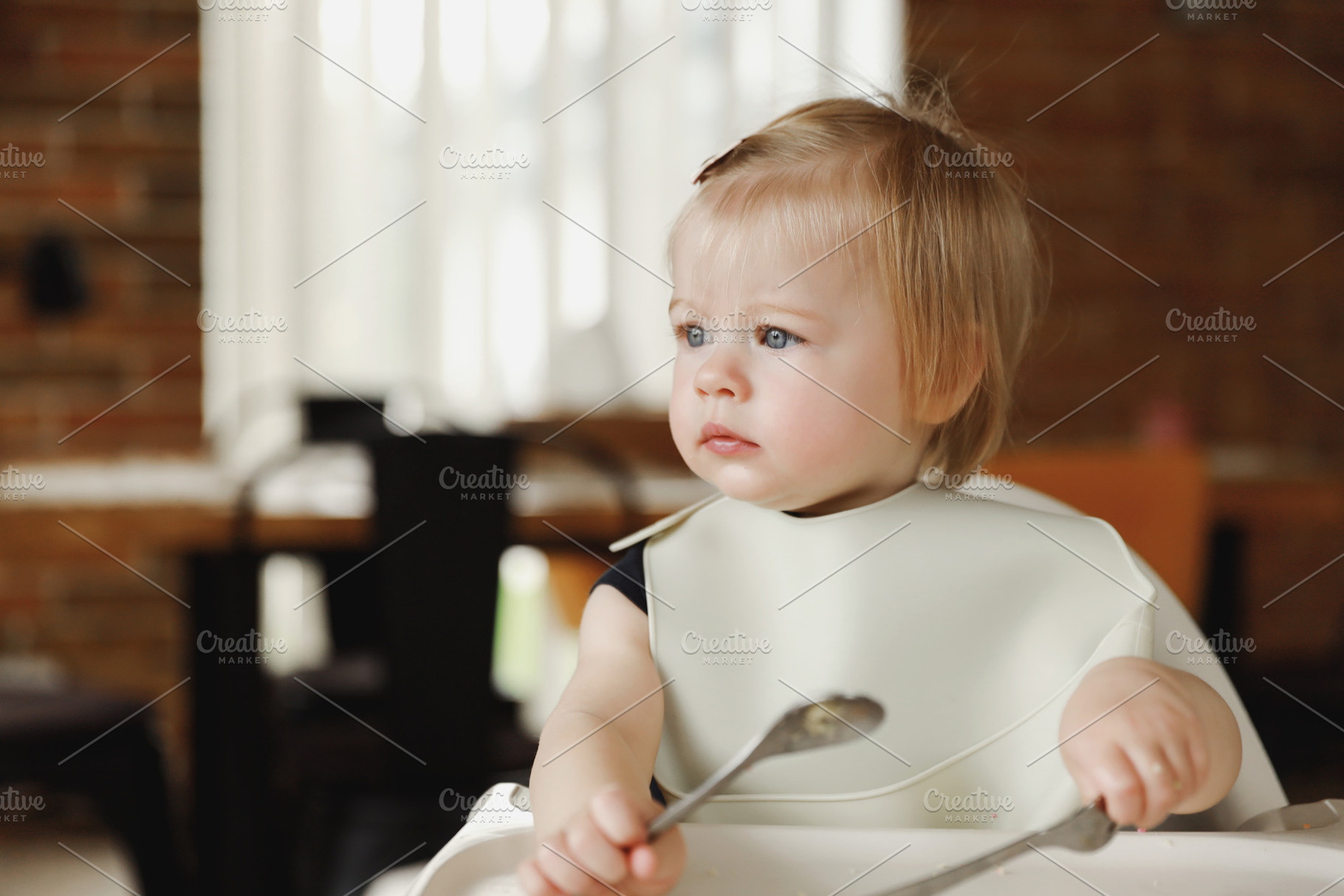 Infant girl or toddler sitting on high chair. Eating food by herself using spoo, a Person Photo by Lenor4ik