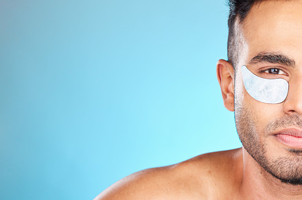 Portrait, skincare and man with eye mask in studio for beauty, grooming and hygiene wellness on blue background.  Face, facial and model relax with eye patch, collagen and skin, cleaning and product, a Photo by Peopleimages.com