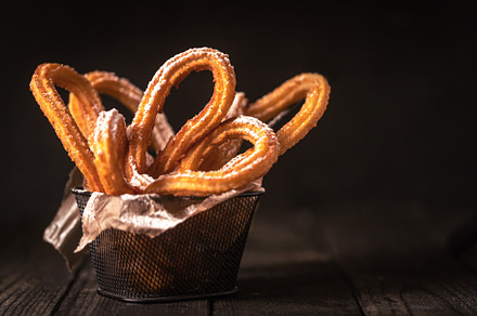 Traditional Spanish churros on the table. Dark and moody photo with copy space, a Food & Drink Photo by zakiroff