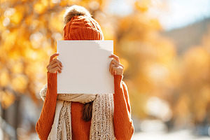 Young woman holding blank poster outdoors in autumn with colorful leaves, a Photo by AlyaAnd