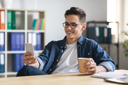 Young Male Office Employee Relaxing With Smartphone And Coffee At Workplace,