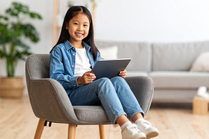 Girl with a tablet sitting on chair at living room while smiling, a Person Photo by DanFLCreativo
