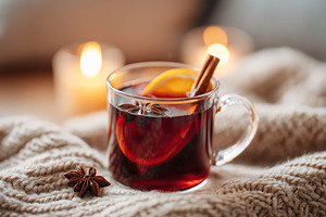 Warm drink with spices and orange slice on cozy blanket beside glowing candles, a Photo by AlyaAnd