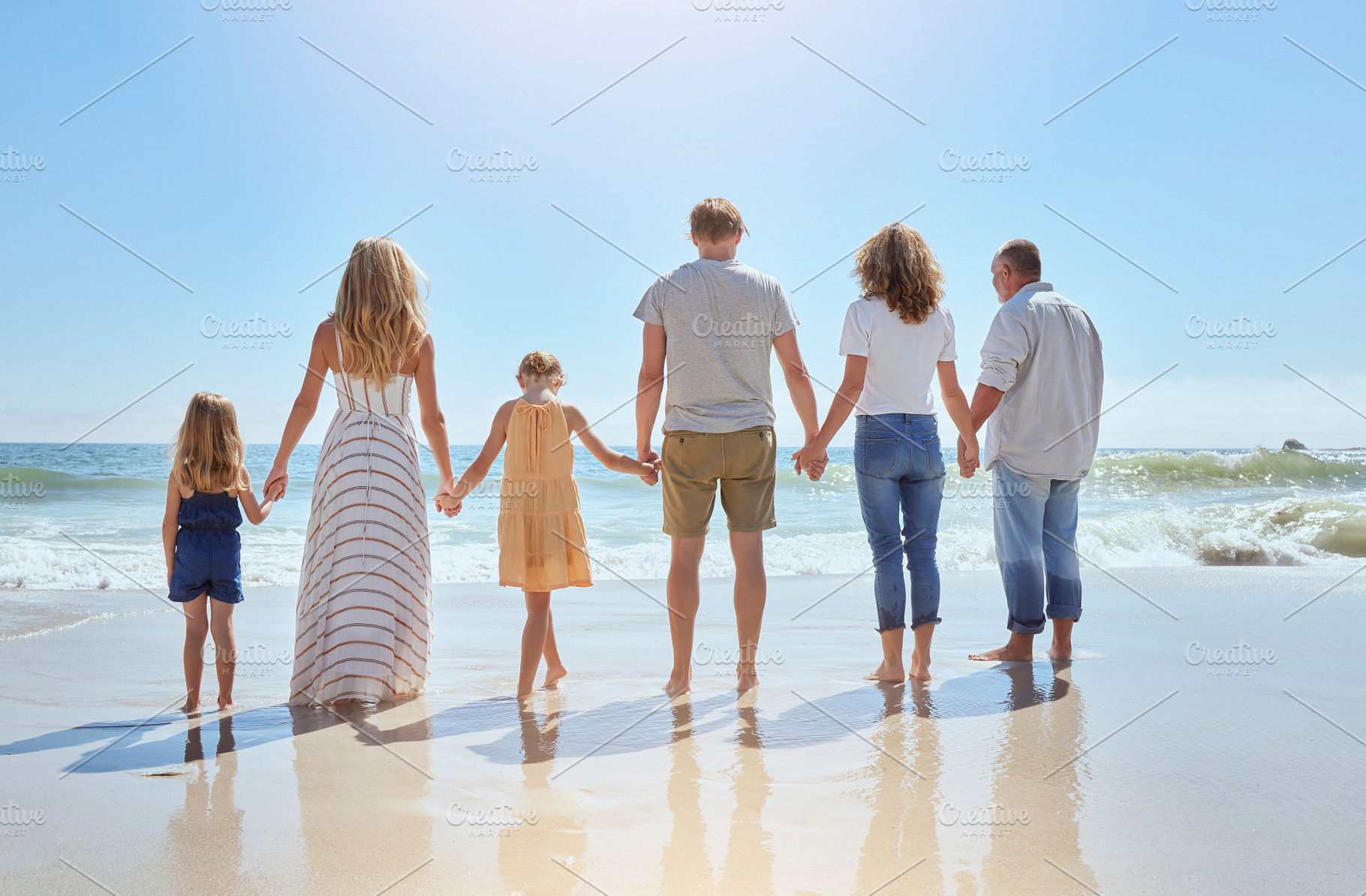 Multi generation family holding hands and walking along the beach together. Caucasian family with two children, two parents and grandparents enjoying summer vacation and standing in the ocean water, a Photo by Peopleimages.com