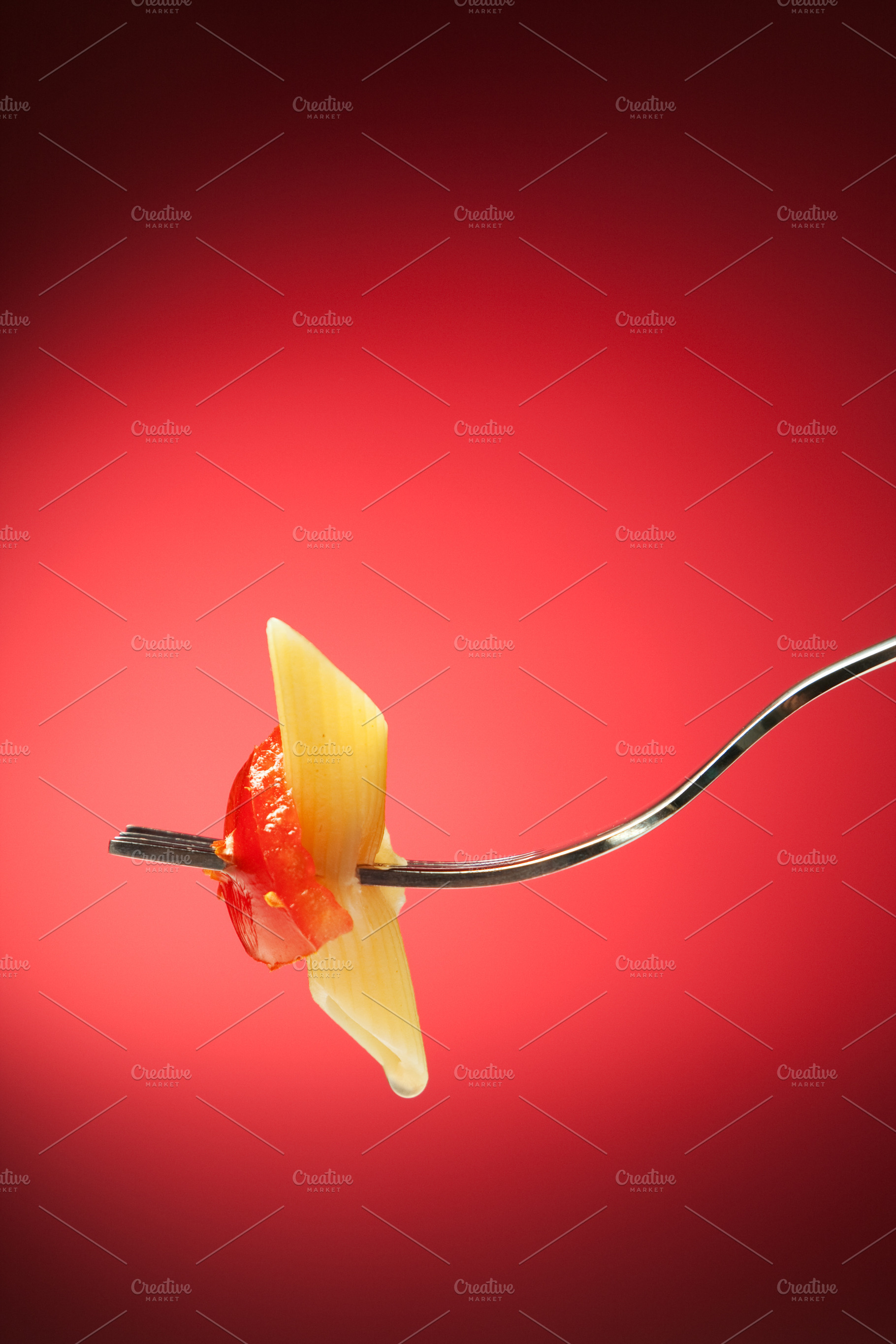 Fork with pasta and tomato on a red background, a Food & Drink Photo by FoodStock