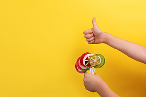 Child's hands holding colorful lollipops and giving a thumbs up, a Food & Drink Photo by Ales Munt