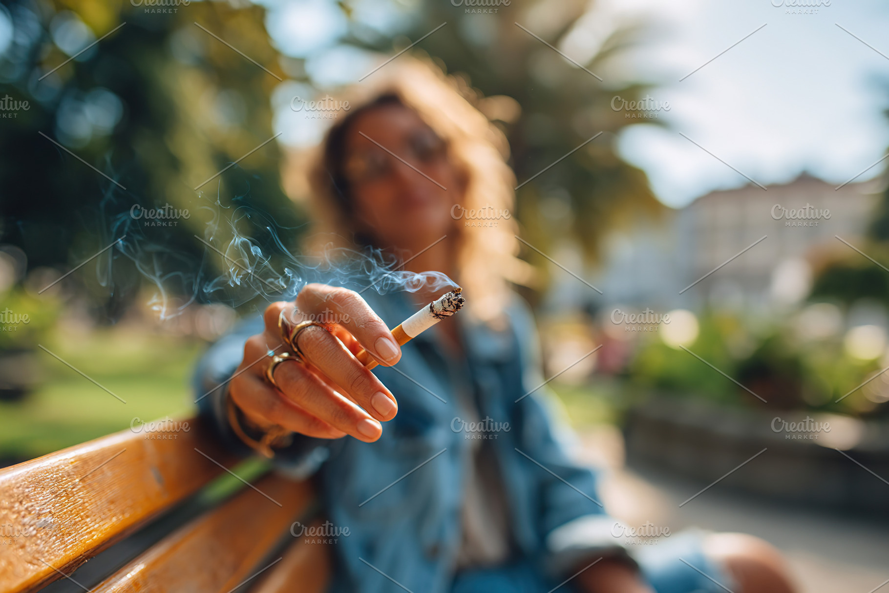 Woman sitting on a bench in a park enjoying a cigarette during a sunny afternoo, a Person Photo by AlyaAnd