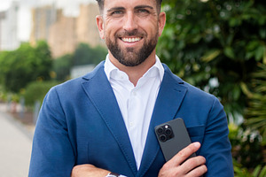 Confident businessman holding smartphone outside modern office building, a Business Photo by etorres69