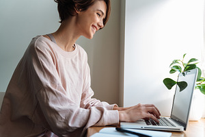 Happy beautiful girl smiling while working with laptop at window