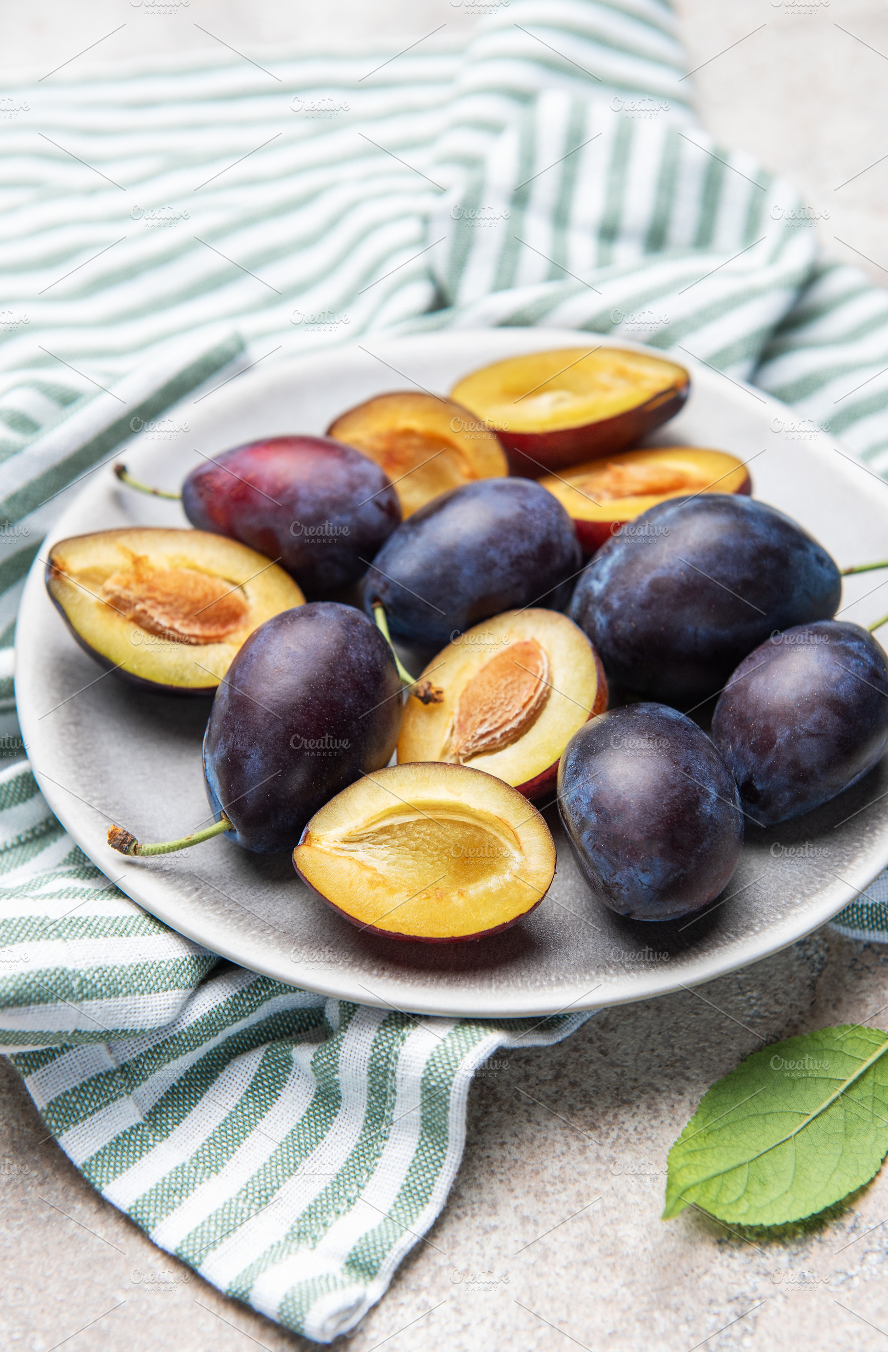 Fresh ripe plums with halves on plate for healthy eating, a Food & Drink Photo by Olena Rudo