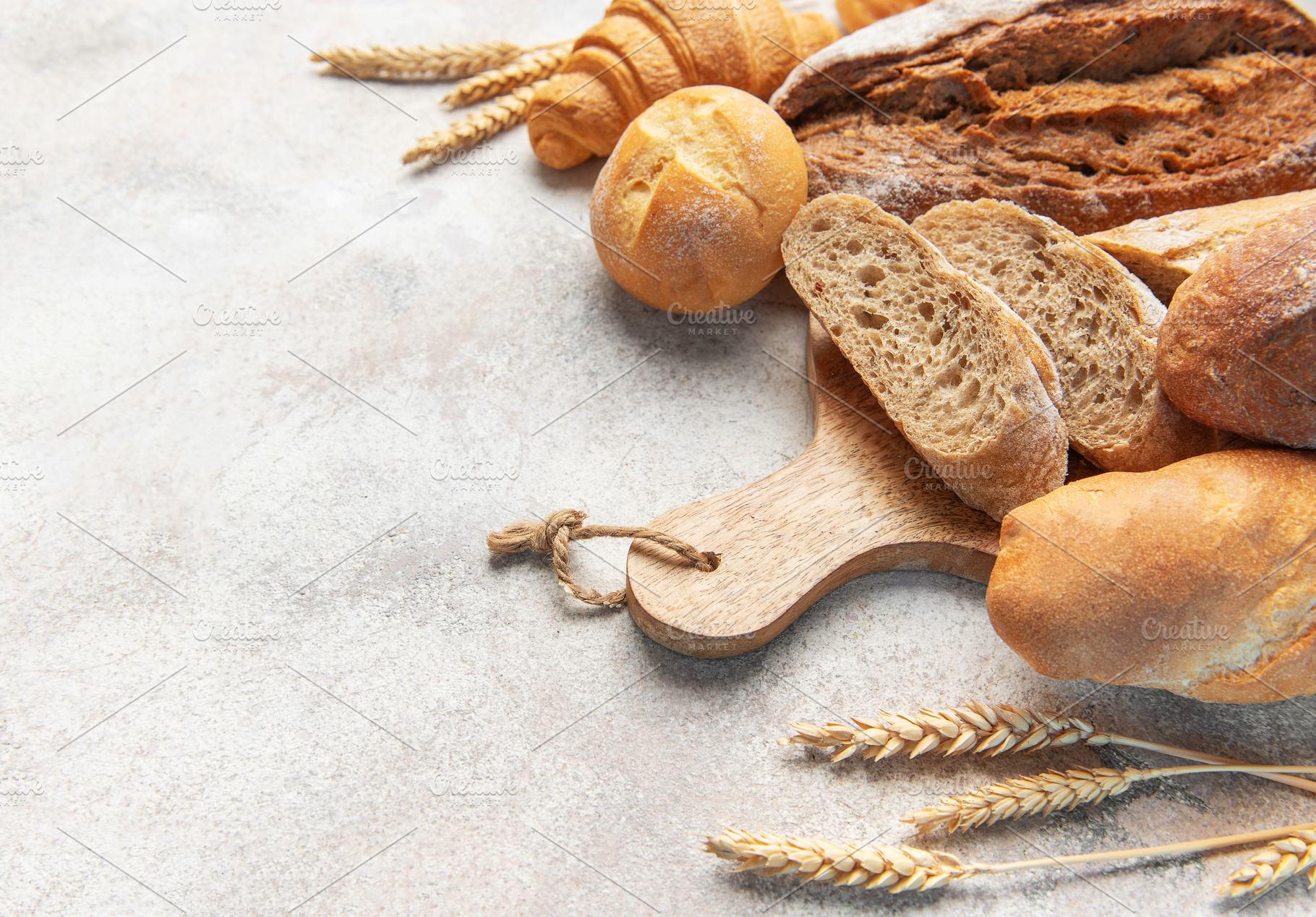 Fresh baked bread assortment with wheat ears on board, a Food & Drink Photo by Olena Rudo