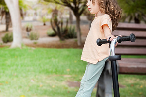 Little girl with curly hair standing on a scooter in the park, a Person Photo by etorres69