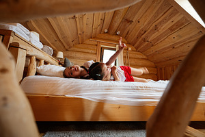 Two children relaxing on a wooden bed in a cozy rustic cabin, a Photo by AS photostudio
