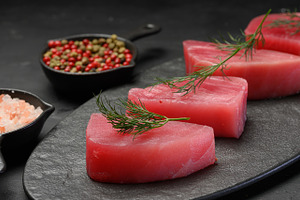 Raw tuna pieces on a black board, decorated with dill sprigs, a Food & Drink Photo by ndanko