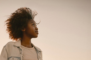 Black woman standing at sunset with city skyline, a Photo by DanFLCreativo