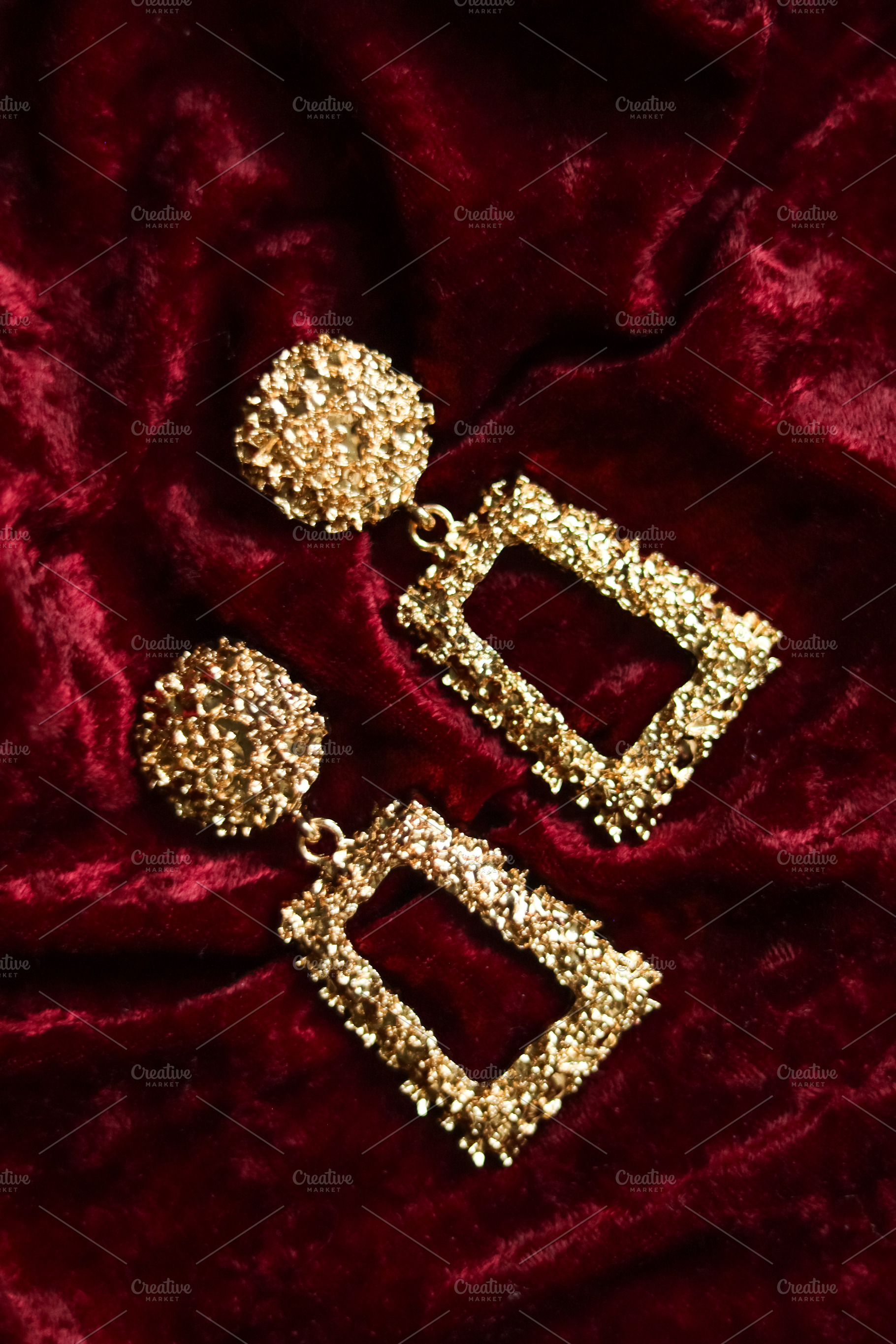 Golden textured dangle earrings showcasing luxury and glamour on a rich red vel, a Photo by Studio ANNA