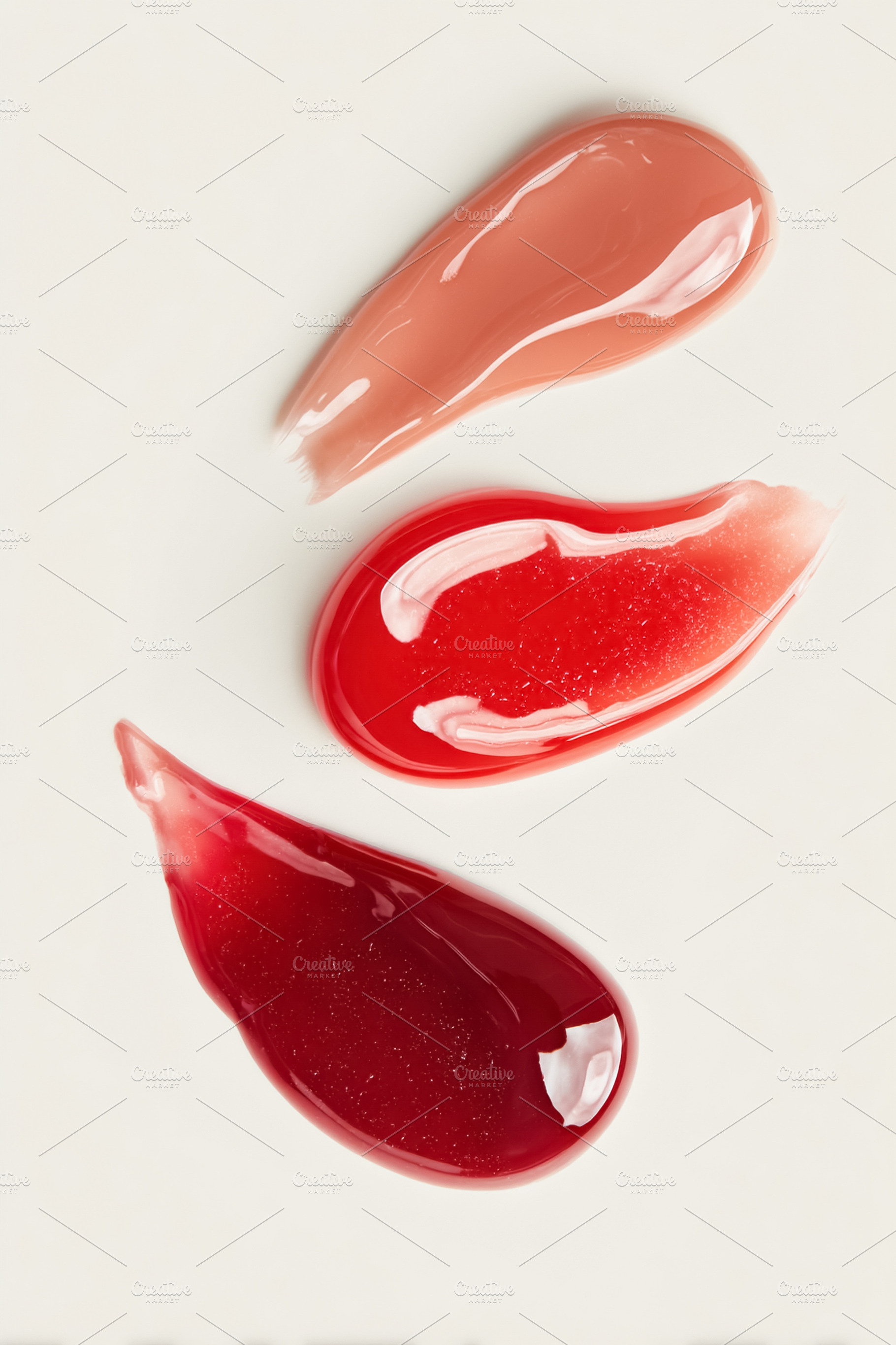 Three glossy lip gloss swatches in shades of nude, red, and berr, a Photo by Studio ANNA