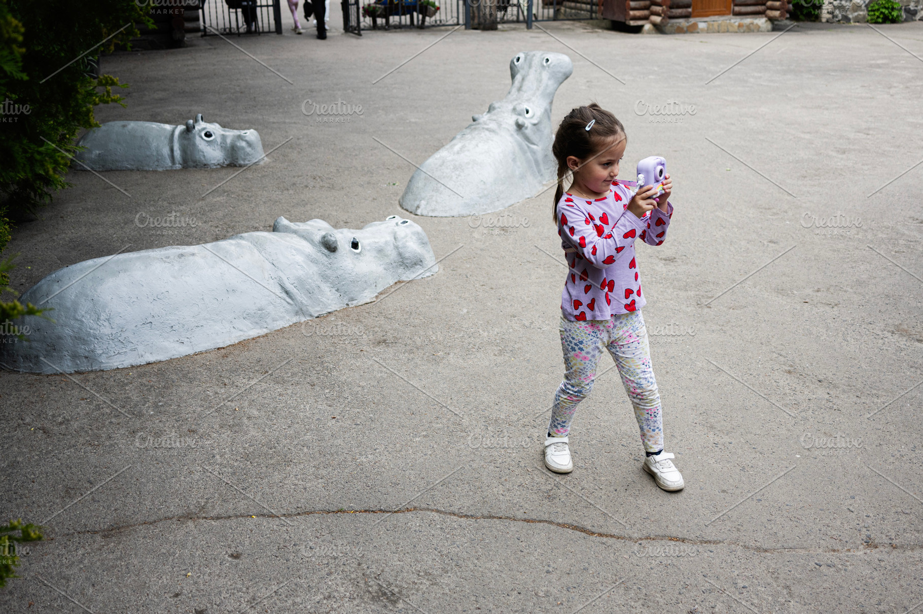 Young girl with camera captures view near submerged hippo sculptures outdoors, a Photo by AS photostudio