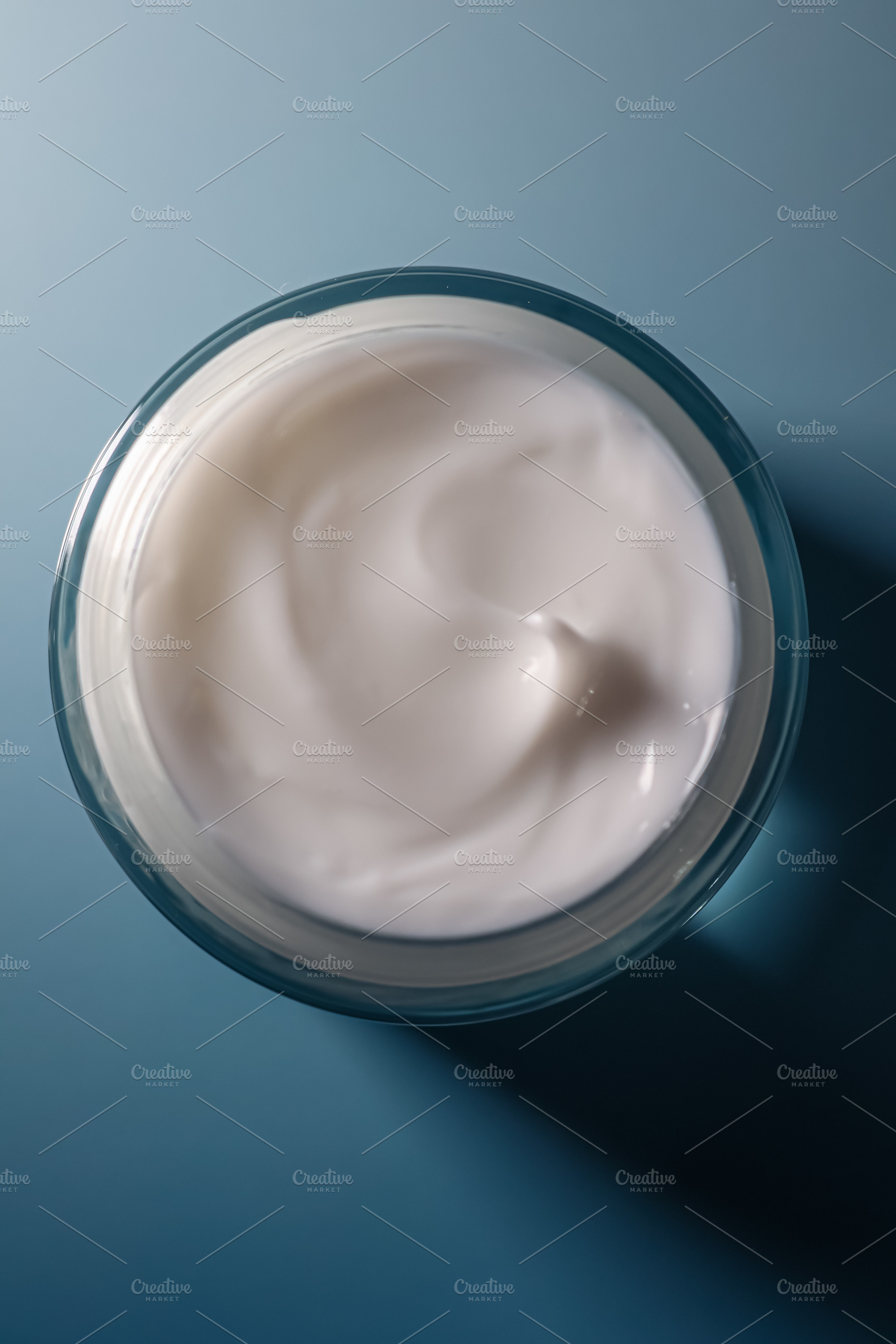 Skincare cream smoothing texture in glass jar on blue background for beauty and, a Photo by Studio ANNA