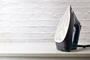 Steam iron on white wooden furniture and white brick background, a Technology Photo by Davizro's Market