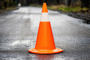 Bright orange road construction cone placed on a wet asphalt roa, an Industrial Photo by AlyaAnd