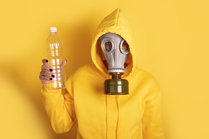 Individual in yellow hoodie and gas mask holding a plastic bottl, a Person Photo by Ales Munt