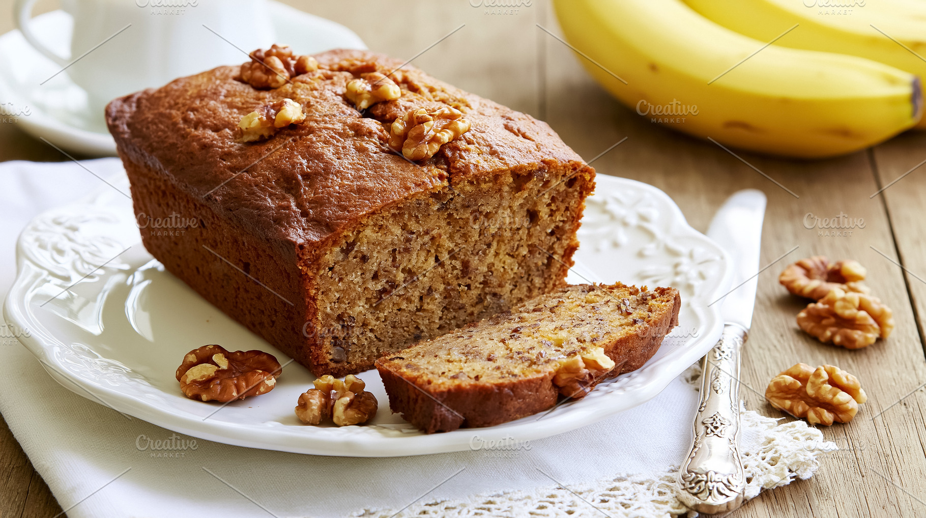 Banana walnut bread loaf, sliced on a white plate with fresh bananas and a knif, a Photo by Studio ANNA